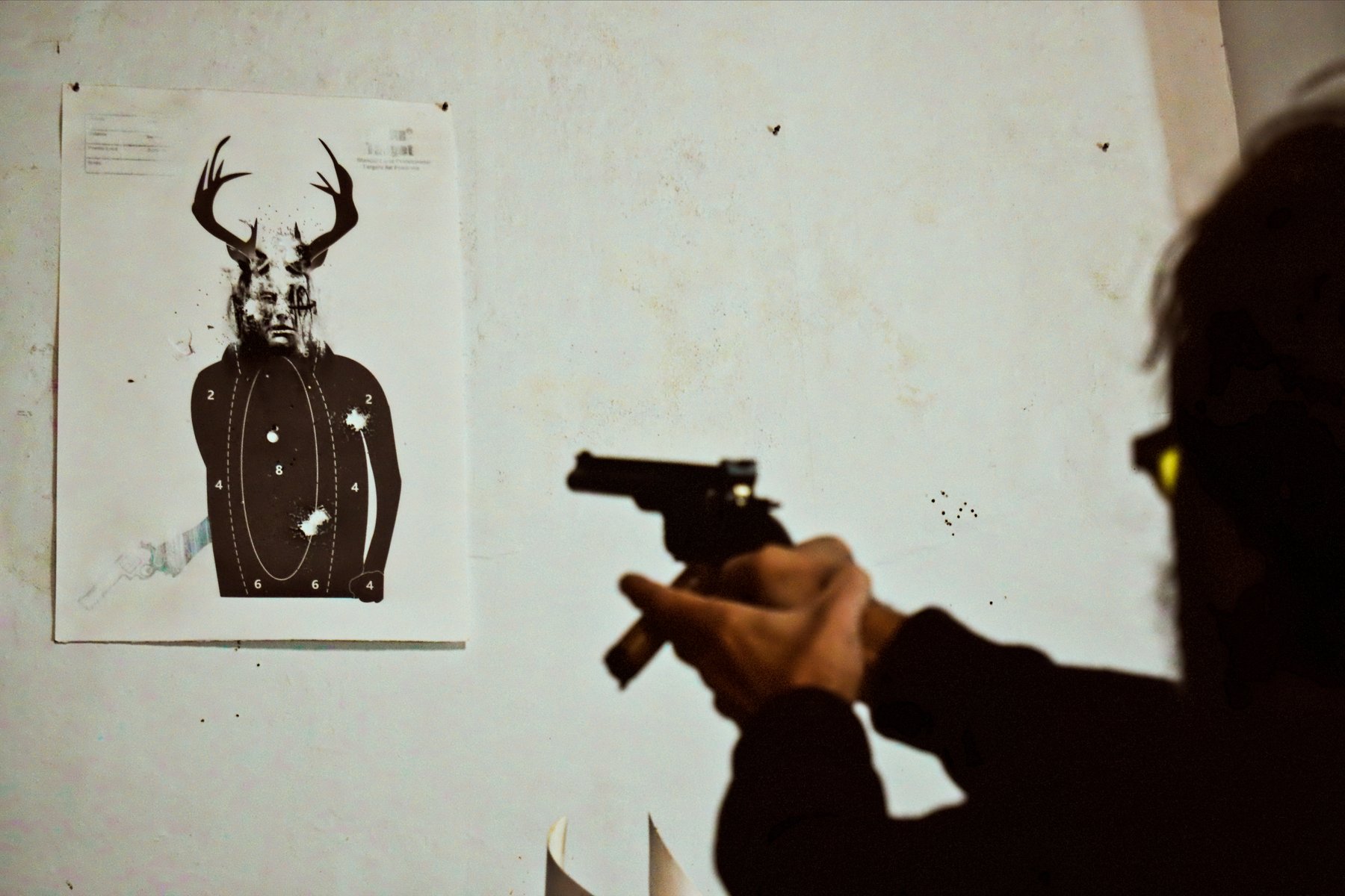 Person aiming a handgun at an indoor shooting range target printed with a stag's antlers