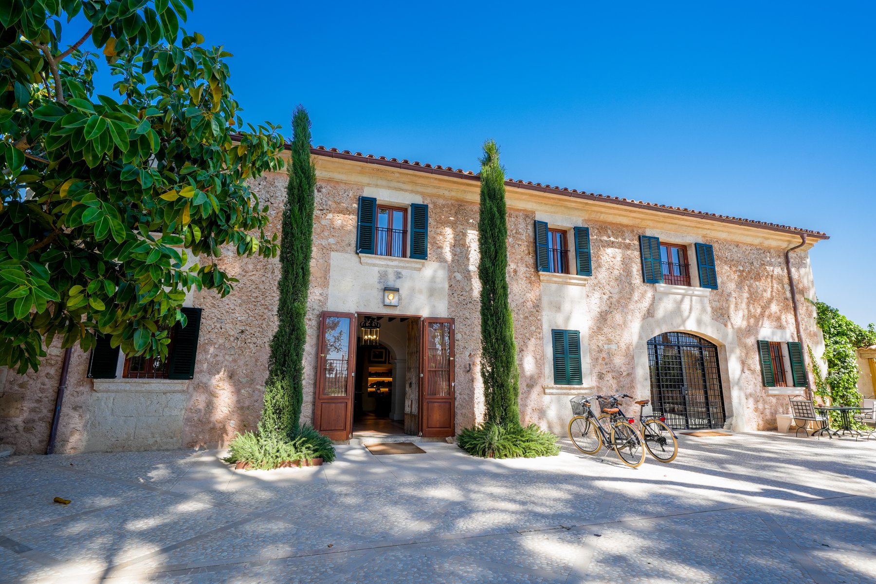 Stone Spanish villa entrance with cypress trees and bicycles parked outside